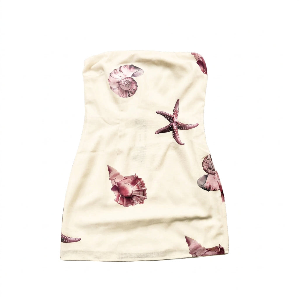 A white strapless baby wrap or towel featuring a print of pink and brown seashells and a starfish, laid flat on a textured white background.